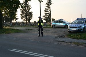 Funkcjonariusz policji dokonuje pomiaru prędkości laserowym miernikiem prędkości, w tle widać stojące radiowozy oznakowane