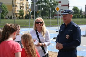 policjant z nauczycielka stoją przed dziećmi na terenie miasteczka ruchu drogowego