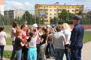 policjant z nauczycielką stoją tyłem wśród dzieci, którym tłumaczą zasady egzaminy