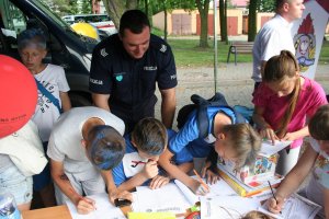 policjant stoi nad dziecmi którzy na stanowisku policyjnym rozwiązują krzyżówkę