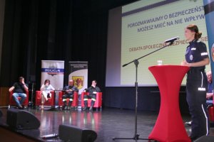 policjantka na scenie zapowiada debat, w tle widać siedzących prelegentów