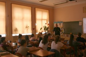 policjant wygłasza swoja prelekcje, słuchaczami sa uczniowie siedzący w ławkach