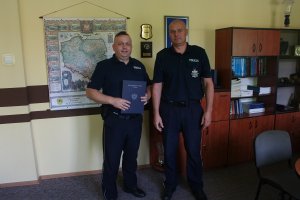 policjant pozuje do zdjęcia z komendantem, w reku trzyma list gratulacyjny