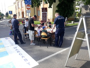 dzieci siedzą przy stolikach , przy nich stoją policjanci