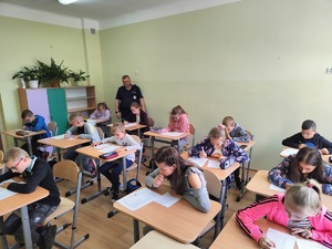 uczniowie piszą test, obok stoi policjant