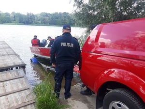 policjant i strażacy wsiadaja do łódki nad jeziorem