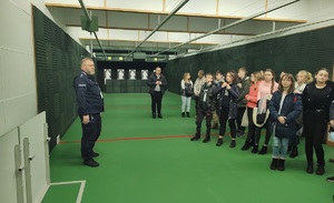 w pomieszczeniu strzelnicy stoi policjant oraz uczestnicy spotkania