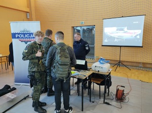 uczestnicy targów stoja przy stanowisku policyjnym i rozmawiają z policjantem