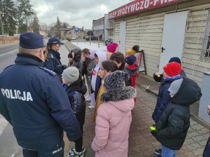 policjanci z dziećmi stoja przed przejściem dla pieszych