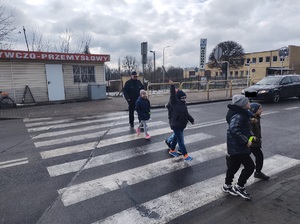 dzieci przechodzą przez przejscie dla pieszych, a za nimi idzie policjant