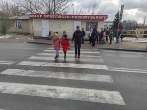 policjantka przeprowadza dzieci przez jezdnie na przejściu dla pieszych