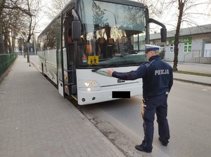 policjant stoi przez autokarek i sprawdza oświetlenie