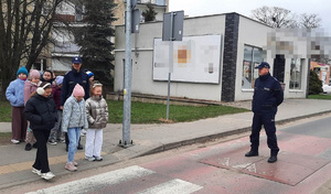 policjant stoi na jezdni i nazoruje przechodzenie dzieci przez jezdnie