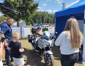 policjant stoi przy motocyklu policyjnym, na którym siedzi chlopczyk