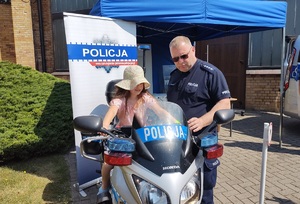 policjant stoi przy dziewczynce siedzacej na policyjnym motocyklu