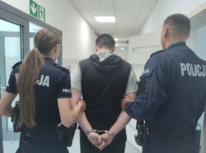 policjanci prowadza zatrzymanego, na rękach ma załozone kajdanki