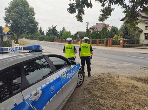 policjanci stoja przy drodze, za nimi stoi radiowóz