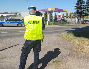 policjant stoi na drodze i mierzy prędkość pojazdów