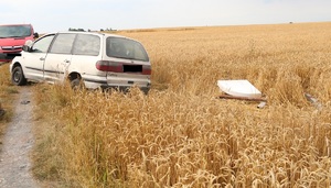 samochód stojący częsciowo na polu a cześciowo na drodze gruntowej
