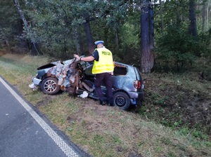 policjant stoi przy rozbitym samochodzie przewróconym w rowie