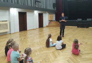 policjantka prowadzi prelekcje na sali, dzieci siedzą na podłodze
