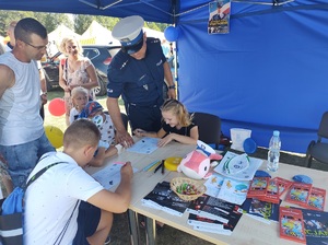 przy stanowisku policyjnym dzieci rozwiązują krzyżówki pod nadzorem policjanta