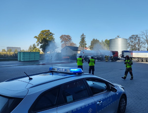 na placy stoja policjanci, strażacy wylewają wode na cysterny