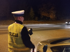 policjant stoi przy radiowozie, w reku trzyma miernika predkosci