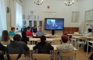 uczniowie siedza wławkach i oglądaja film który jest wyświetlany na ekranie