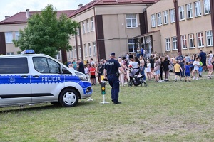 policjant stoi przy radiowozie, obok stoja znali drogowe