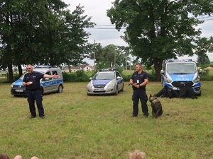 dwóch policjantów na tle samochodów stoi przed dziećmi