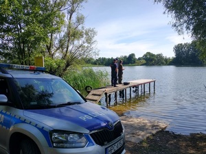 dwóch policjantów i strażnik stoja na pomoście nad jeziorem