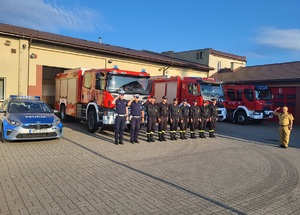 dwóch policjantów stoi przy strazakach i oddają hołd