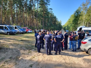 policjanci i strażacy stoja w lesie na odprawie