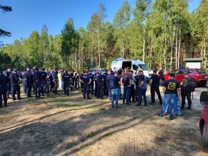 policjanci i strażacy stoja zebrani w lesie