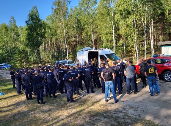 policjanci i strażacy stoja w lesie przey samochodzie