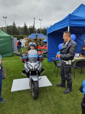 jedno dzieci siedzi na policyjnym motocyklu, obok stoi policjant