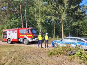 policjanci stoja przez pojazdem strazackim i zabezpieczają droge