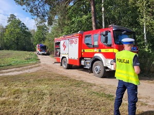 policjant stoi przy drodze i zabezpiecza wóz strażacki