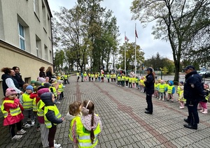 dwóch policjantów stoi przed dziecmi na placu i prowadzi prelekcje