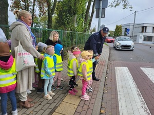 policjant stoi z dziecmi przed przejściem dla pieszych i pokazuje reka na samochody