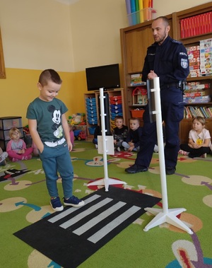 policjant przy uzyciu maty i switeł pokazuje jak przechodzic przez jezdnie