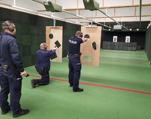 dwóch policjantów w pozycji kleczacej i stojącej oddaje strzały zza przesłony z trzema otworami