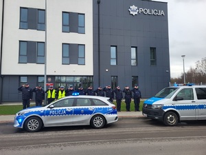 przed budynkiem policji stoja policjanci, którzy oddaja honor, przed nimi stoja radiowozy z włączonymi sygnałami świetlnymi