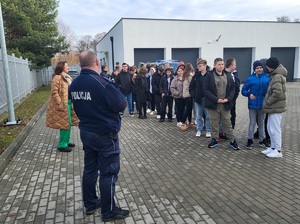 policjant stoi przed uczestnikami przed budynkiem