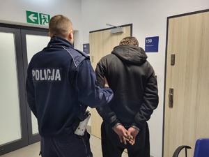 policjant trzyma zatrzymanego, który ma założone kajdanki na rece trzymane z tyłu