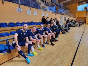 policjanci w strojach sportowych siedza na ławce rezerwowych podczas meczu