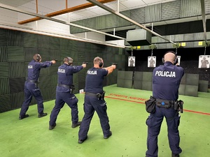 czterech policjantów stoi przed tarczą i oddaja strzały