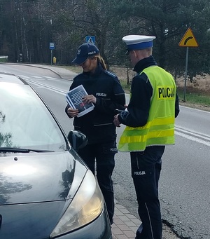 dwóch policjantów stoi przy kontrolowanym pojeździe, policjantka trzyma w reku ulotki