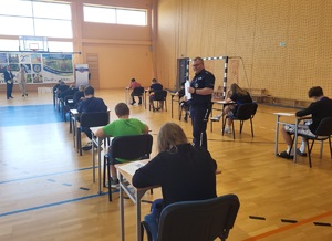 policjant chodzi pomiędzy uczniami, którzy rozwiazuja testy